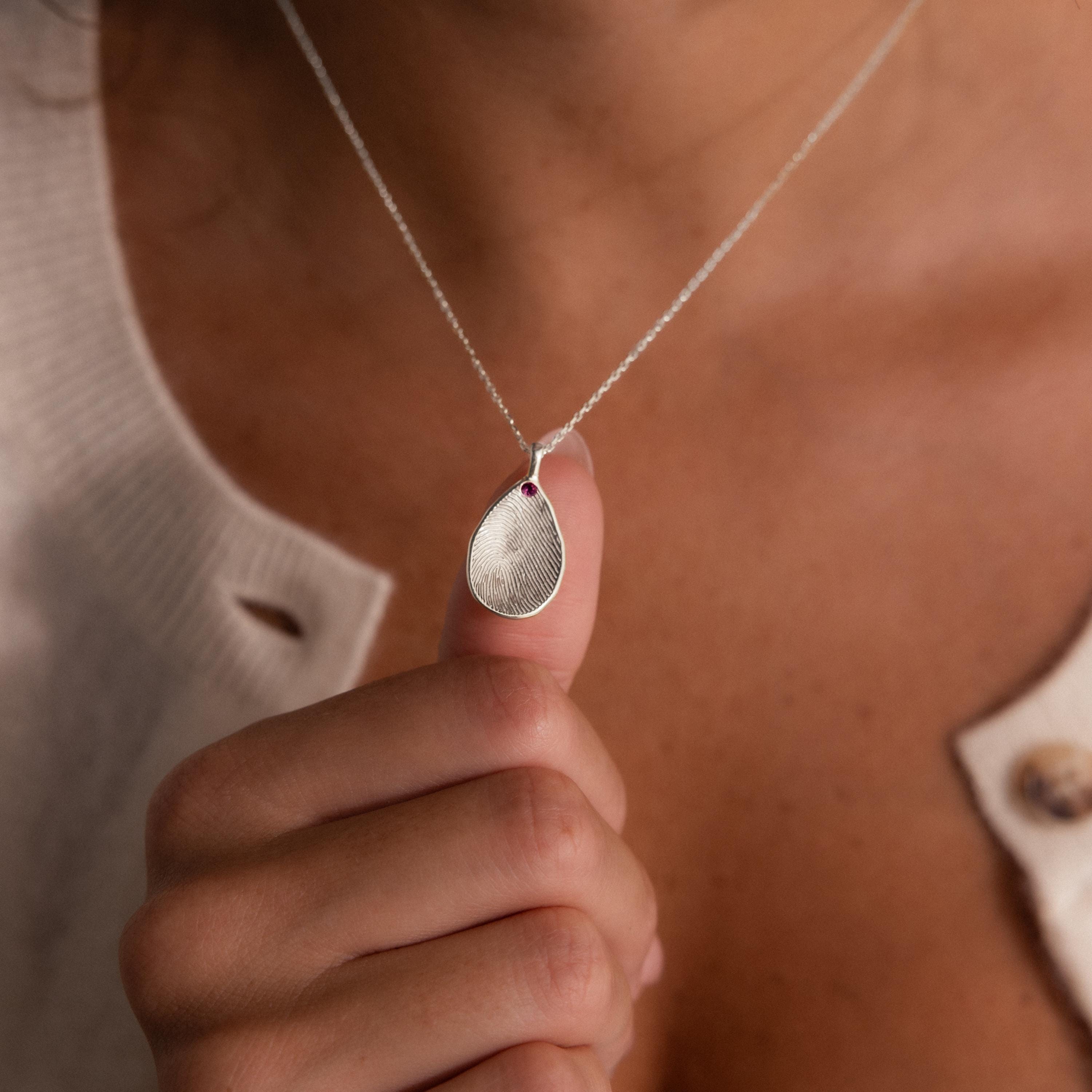 A person holds the Fingerprint Birthstone Teardrop Necklace in Sterling Silver, featuring a fingerprint design and small gemstone for a personalized jewelry piece.