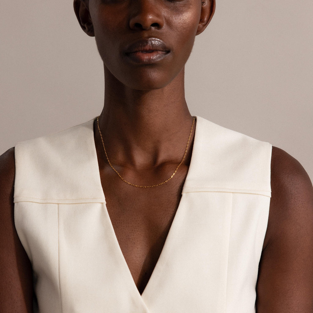 A woman shown from the shoulders up wears a sleeveless white top and the Dainty Paperclip Necklace in 18K Gold.