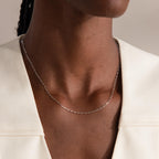 Close-up of a person wearing the Dainty Paperclip Necklace in Sterling Silver, an elegant piece of modern jewelry, paired with a cream-colored top.