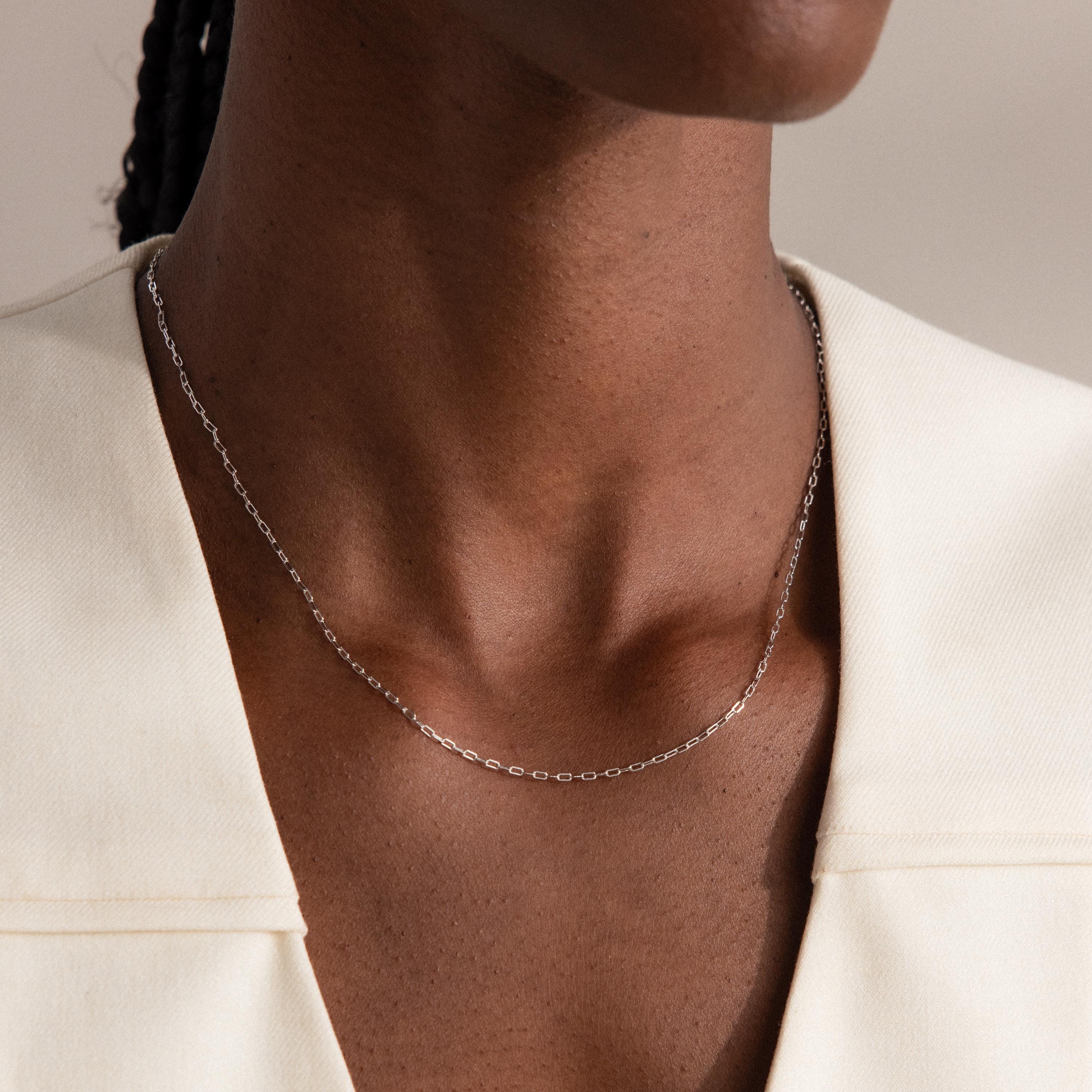 Close-up of a person wearing the Dainty Paperclip Necklace in Sterling Silver, an elegant piece of modern jewelry, paired with a cream-colored top.