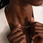 A person in a white blazer holds the Dainty Herringbone Necklace in 18K Gold delicately with both hands.