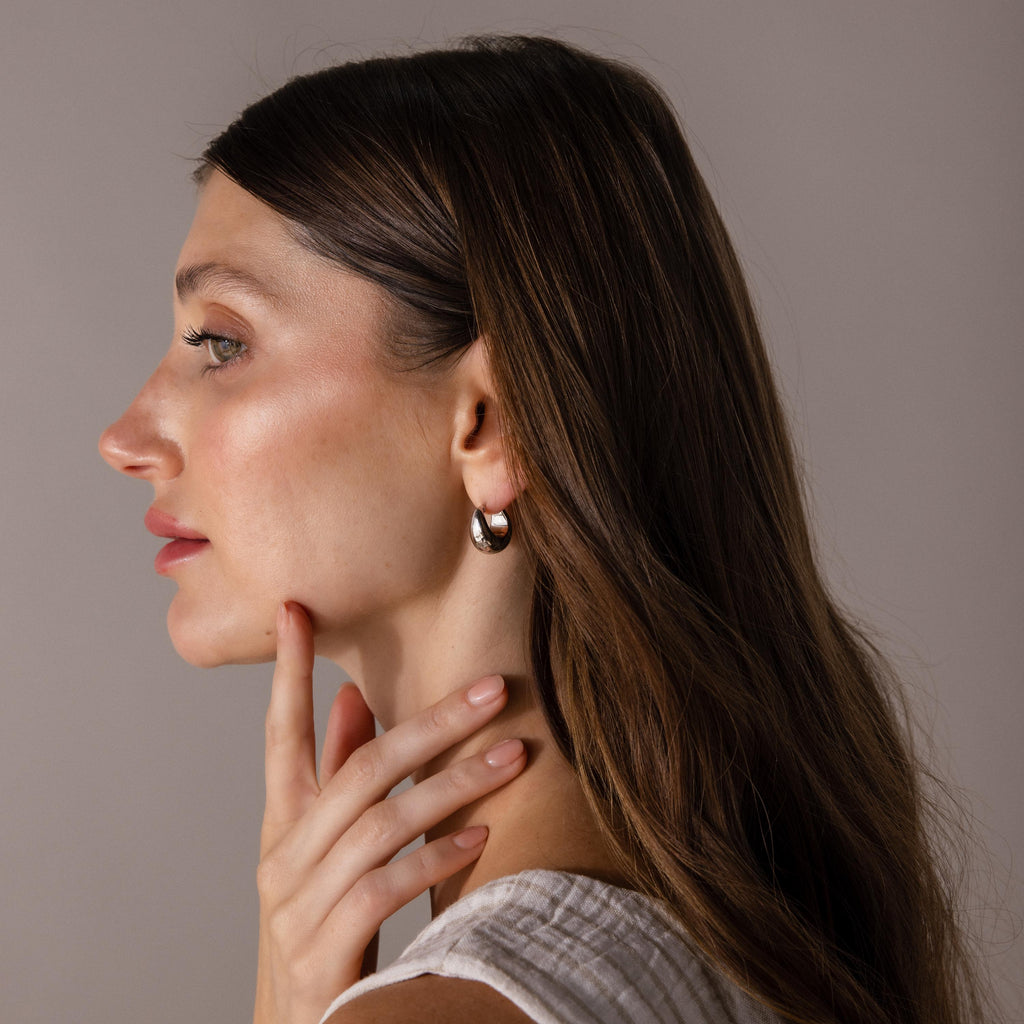Woman with long brown hair wears a white top and Bold Teardrop Earrings in White Gold, touching her chin in side profile.
