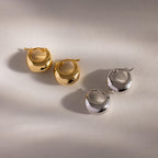 A pair of Bold Teardrop Earrings in gold and silver rests on a light surface with soft shadows—ideal for mixing and matching with other statement pieces for a contemporary jewelry style.