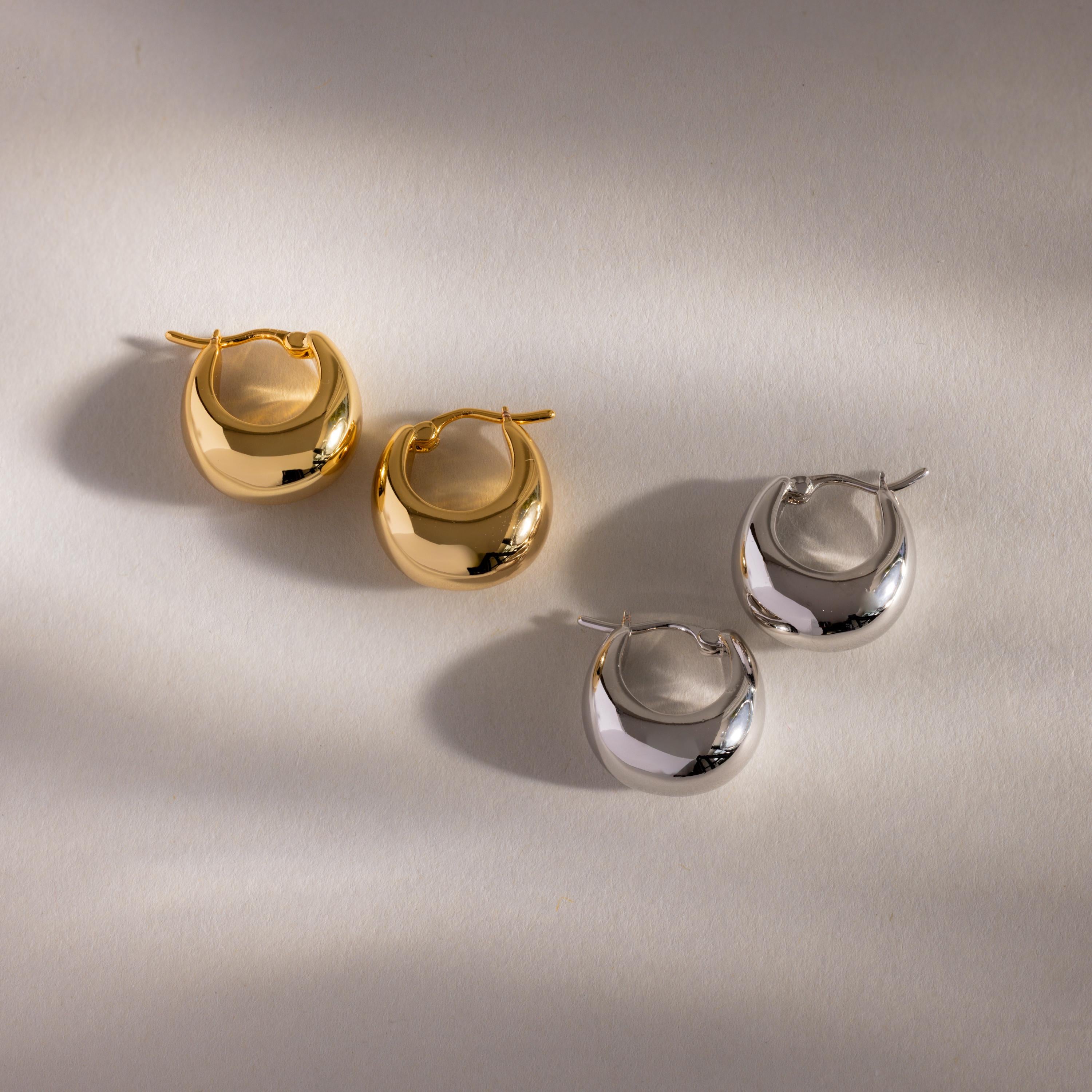 A pair of Bold Teardrop Earrings in gold and silver rests on a light surface with soft shadows—ideal for mixing and matching with other statement pieces for a contemporary jewelry style.