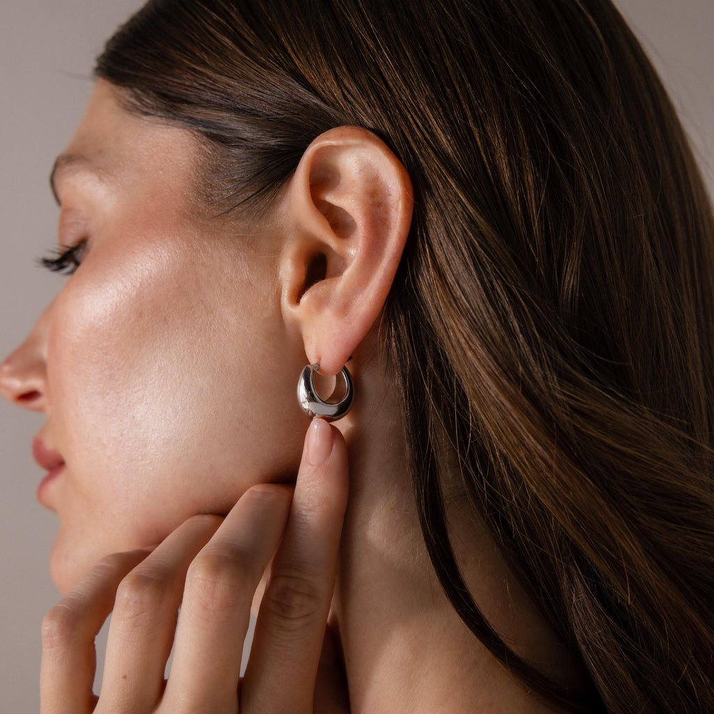 A woman with brown hair tucked behind her ear showcases Bold Teardrop Earrings, highlighting their modern and shiny silver design.
