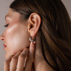 A woman with brown hair tucked behind her ear showcases Bold Teardrop Earrings, highlighting their modern and shiny silver design.