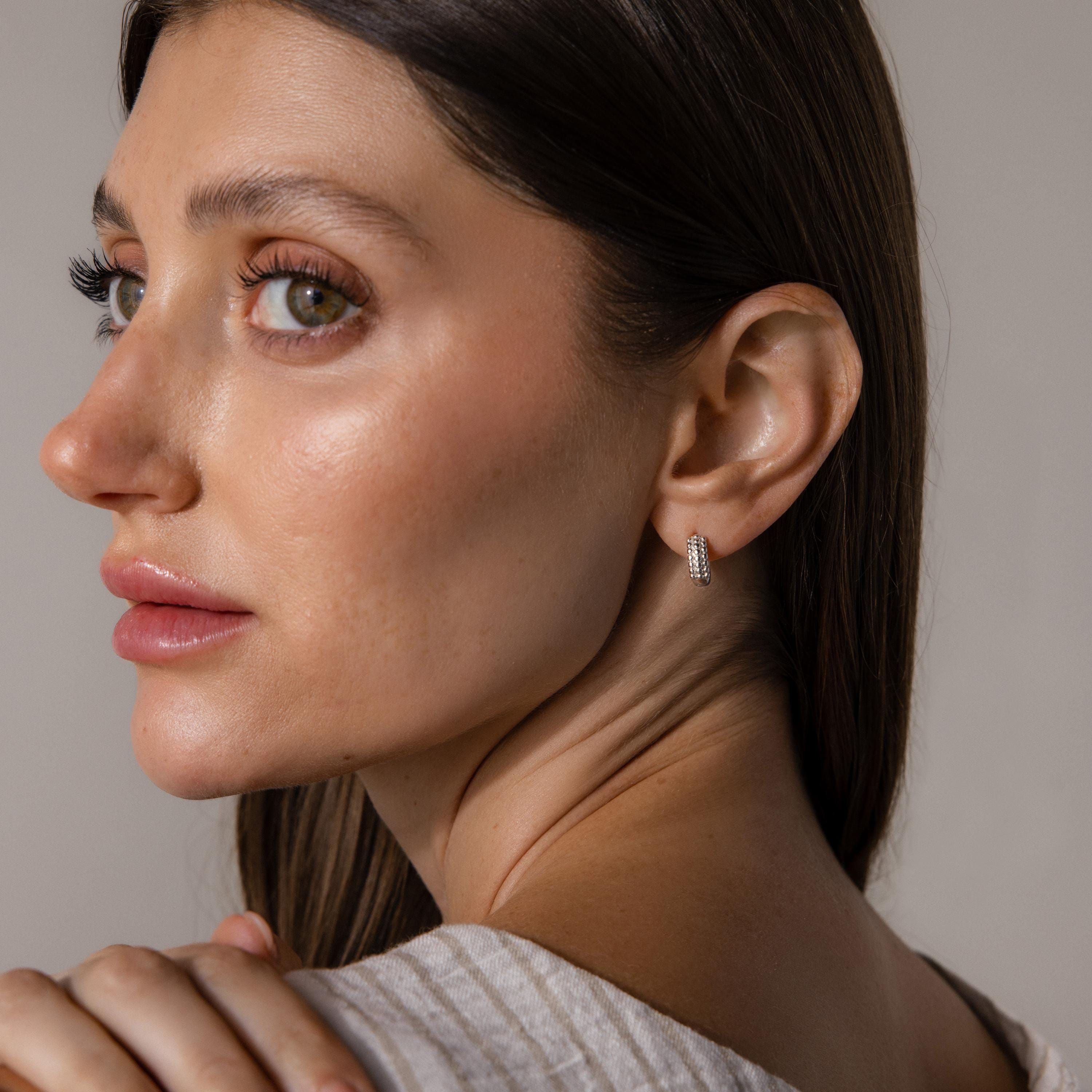 A woman with long brown hair wears Beaded Chunky Hoops, looking over her shoulder against a neutral background.