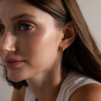 Woman with long brown hair gazes to the side in soft lighting, wearing Beaded Chunky Hoops in 18K Gold.