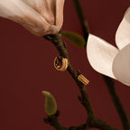 The Beaded Chunky Hoops in 18K Gold are displayed on a magnolia branch with white flowers, set against a deep red background.