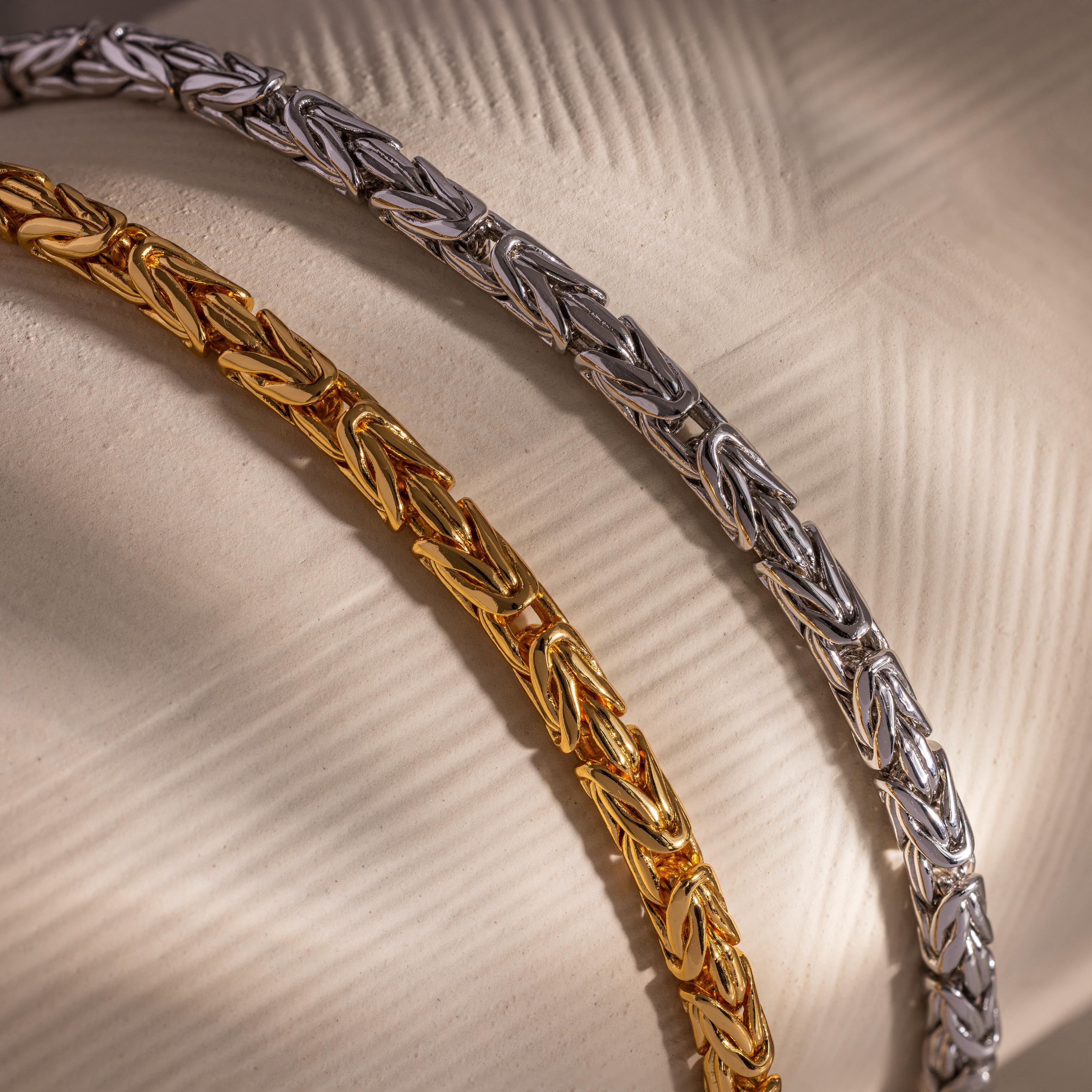 The Byzantine Link Bracelet features an intricate interwoven design, creating a stunning statement piece showcased on a textured beige surface.