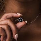A hand holds the Onyx Star Pendant Necklace in Sterling Silver, featuring an elegant star design, displayed against a black background.
