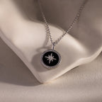The Onyx Star Pendant Necklace in Sterling Silver features a round black onyx pendant with a star design, shown on a white ceramic surface.
