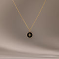 The Onyx Star Pendant Necklace in 18K Gold features a circular black onyx pendant with a star design, creating a striking celestial look against a neutral background.