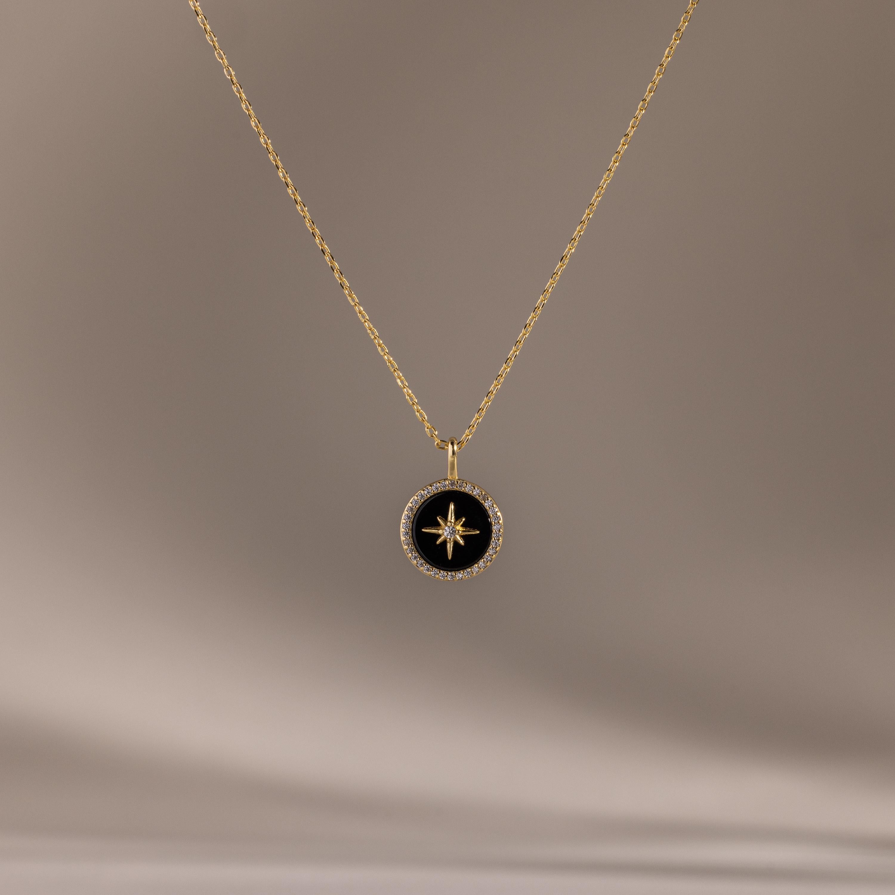 The Onyx Star Pendant Necklace in 18K Gold features a circular black onyx pendant with a star design, creating a striking celestial look against a neutral background.