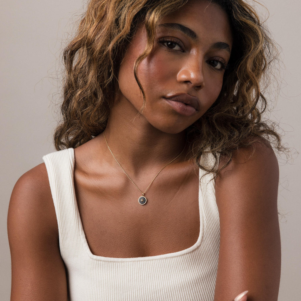 A woman with wavy hair in a cream tank top wears the Onyx Star Pendant Necklace and looks at the camera.