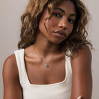A woman with wavy hair in a cream tank top wears the Onyx Star Pendant Necklace and looks at the camera.