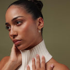 Model showcasing our Pave Bow Charm Hoops styled with diamond studs against a green background