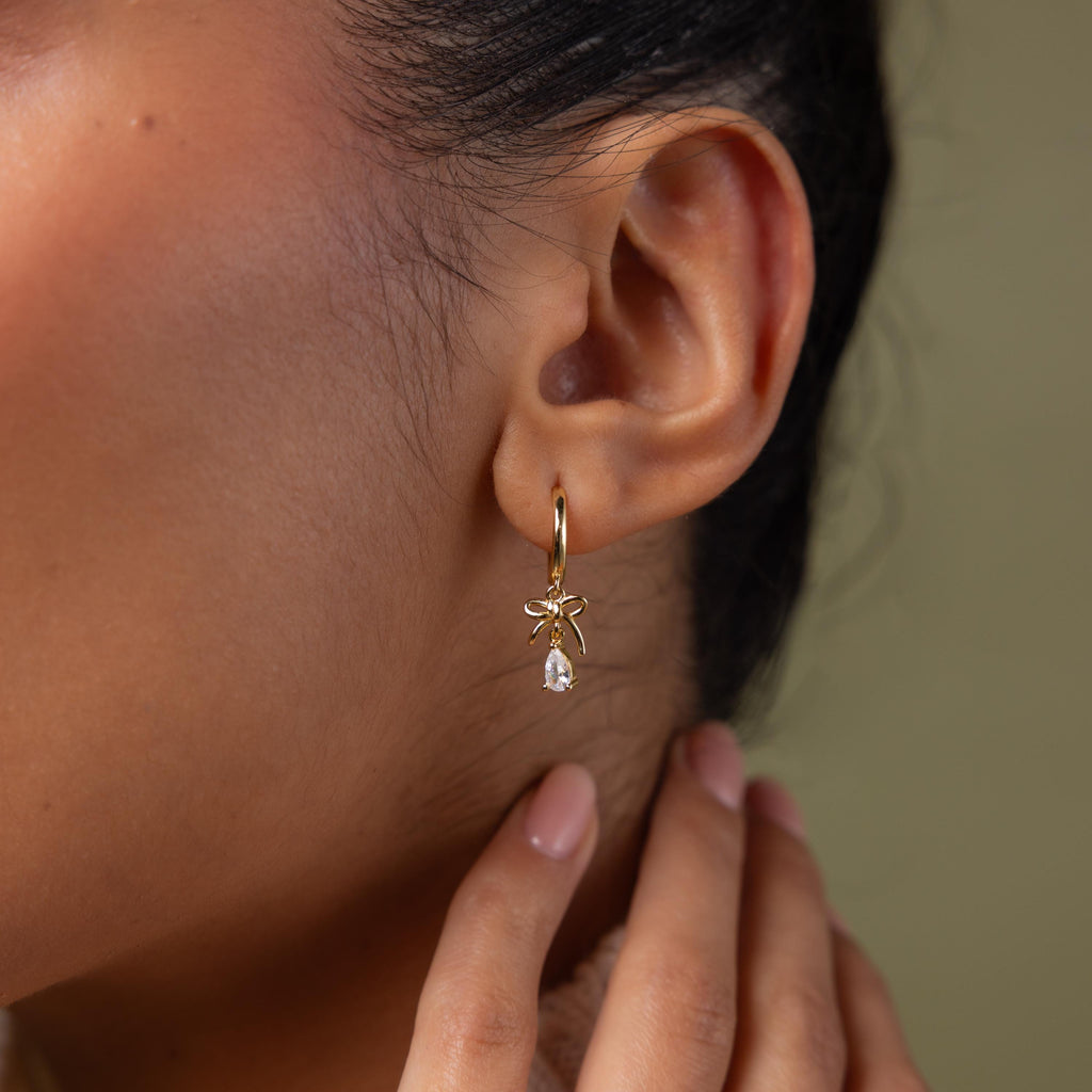 Close-up of a model wearing our Teardrop Ribbon Charm Hoops in gold 