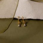 Flatlay of our Teardrop Ribbon Charm Hoops in Gold against a white and green background