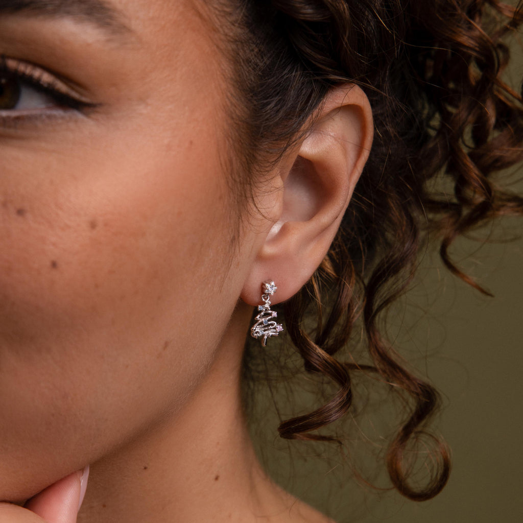 Close-up of a model wearing our Holiday Diamond Tree Studs in Silver with a green background