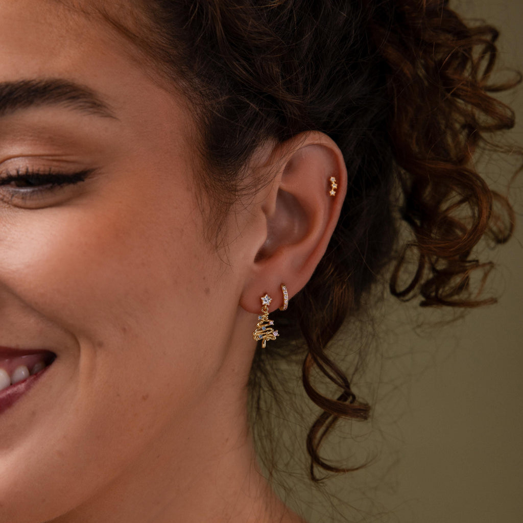 Close-up of a model wearing our Holiday Tree Studs in gold, styled with our Coco pave huggies and star studs