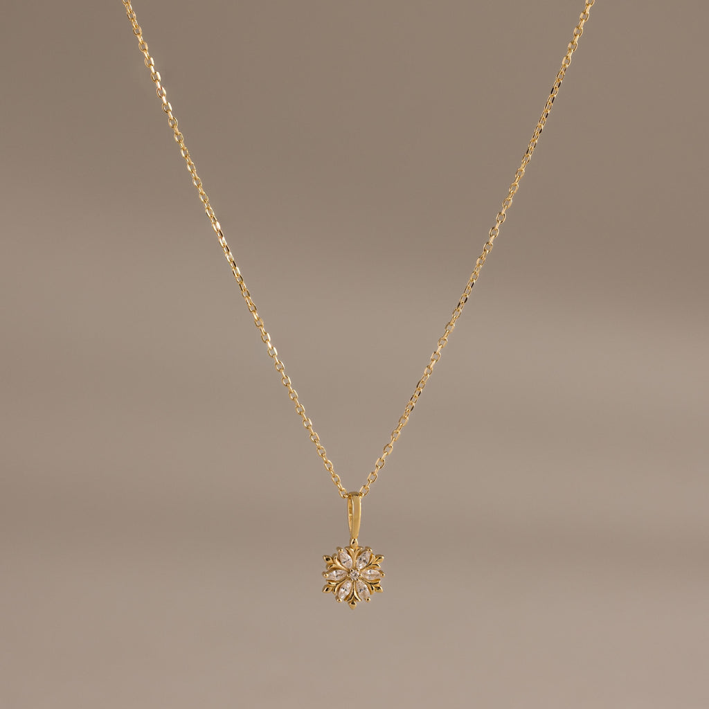 Flatlay of our Diamond Poinsettia Pendant Necklace in Gold on a brown background