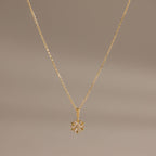 Flatlay of our Diamond Poinsettia Pendant Necklace in Gold on a brown background