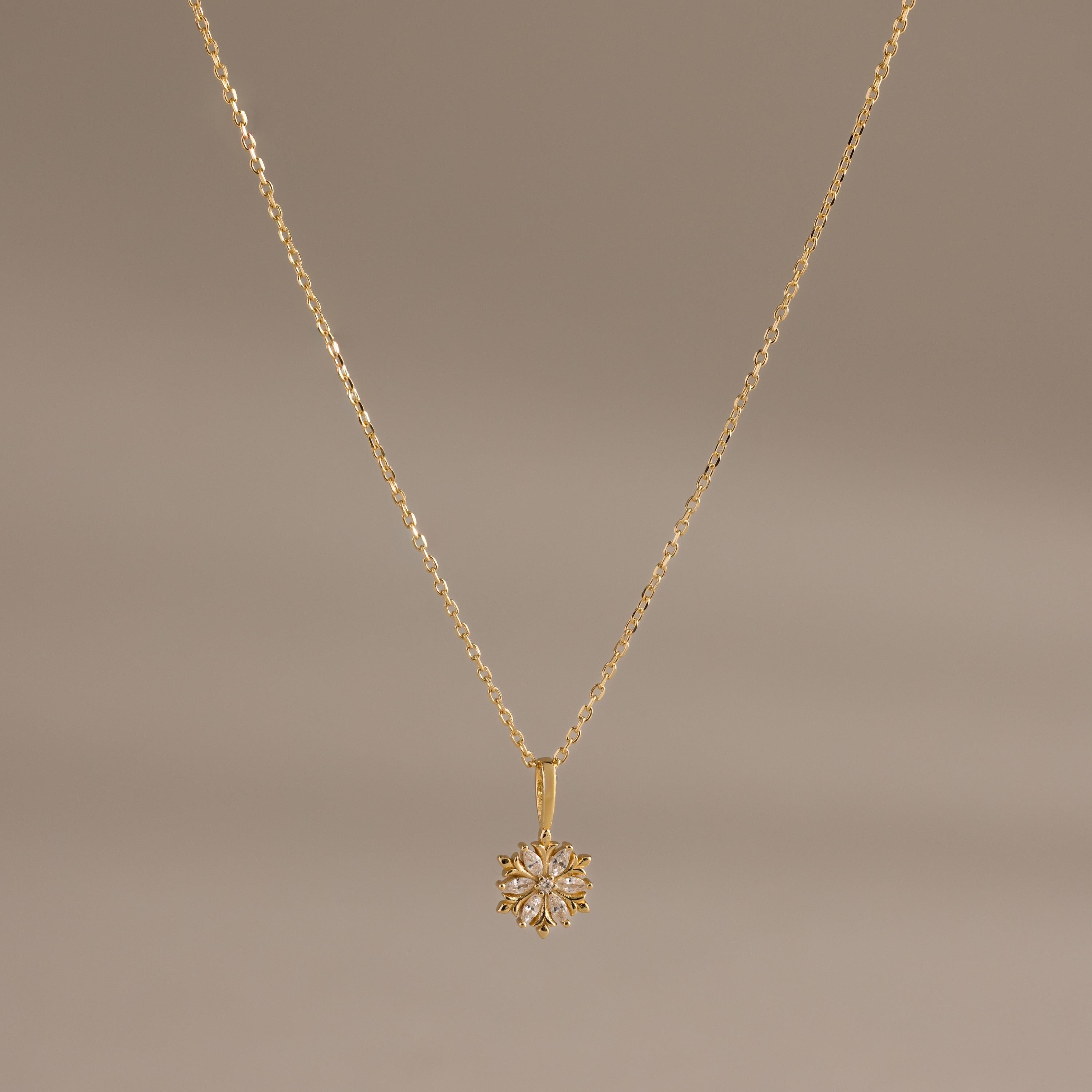 Flatlay of our Diamond Poinsettia Pendant Necklace in Gold on a brown background
