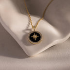 The Onyx Star Pendant Necklace in 18K Gold features a black onyx star and celestial design, displayed on a white sculpted surface. Ideal for anyone who loves elegant cosmic-inspired jewelry.