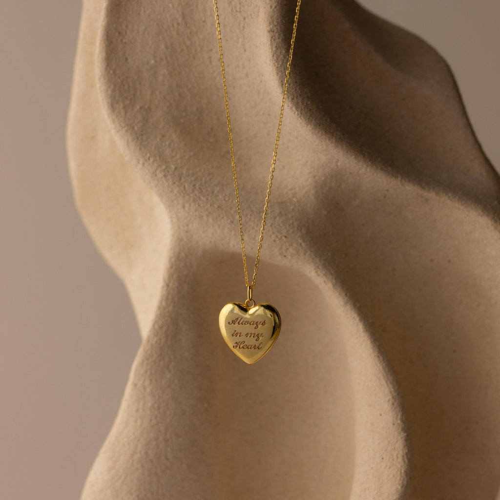 Flatlay of our Engraved Heart Locket Necklace in 18K Gold