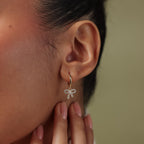 Close-up of an ear wearing a gold diamond bow hoop earrings against a neutral background.