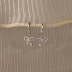 Flatlay of our Pave Bow Charm Hoops
 in Silver on a beige fabric background