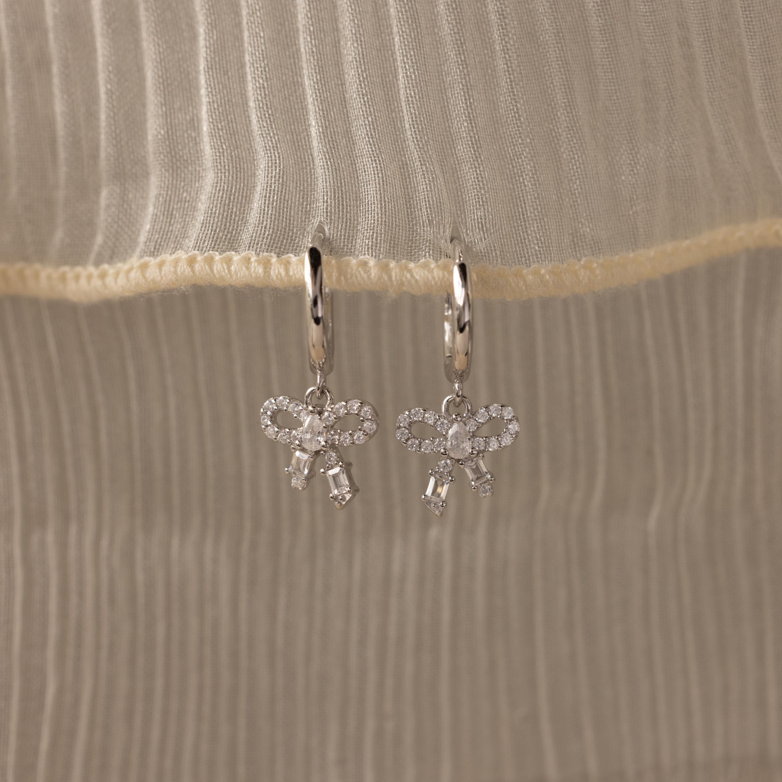 Flatlay of our Pave Bow Charm Hoops
 in Silver on a beige fabric background