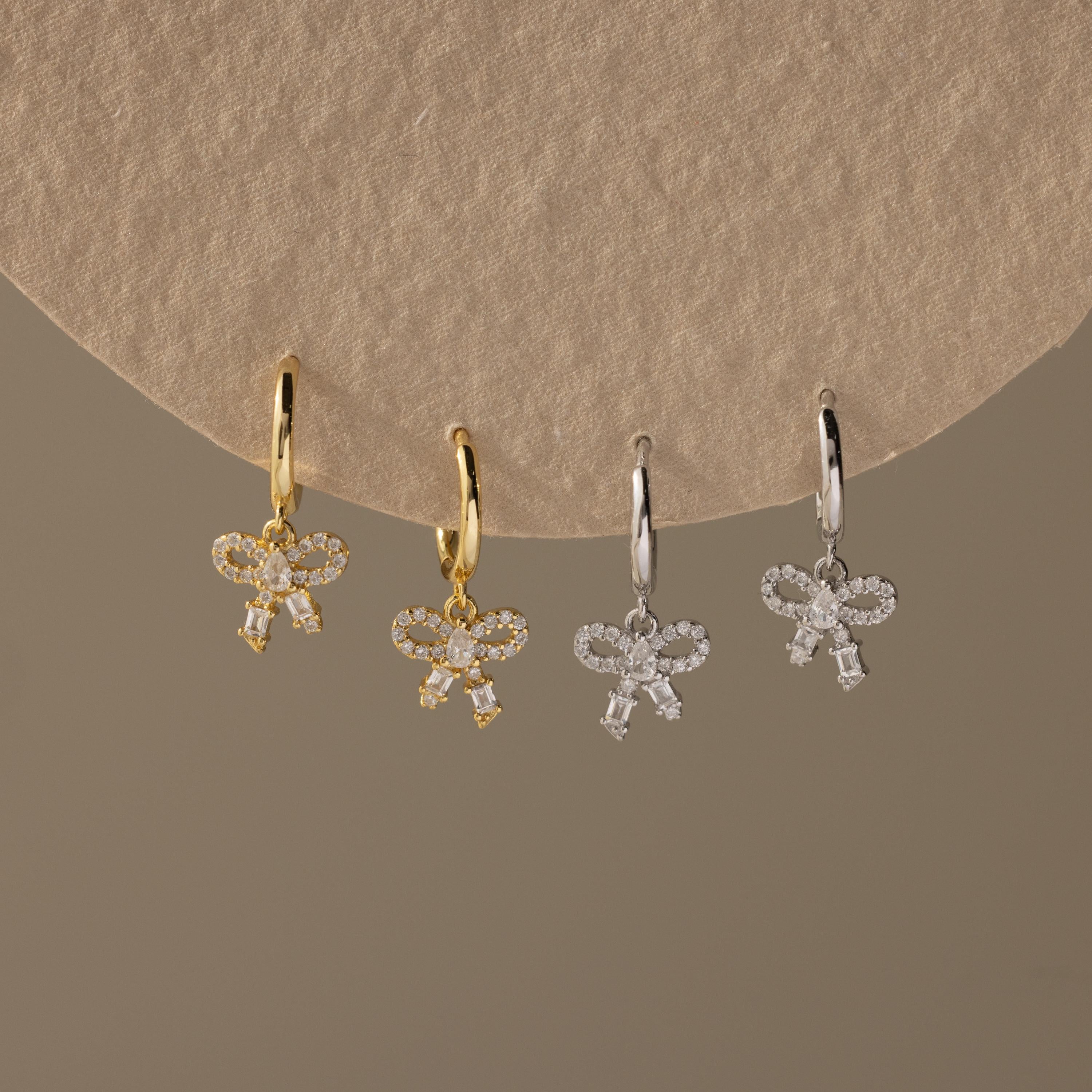 Flatlay of 2 pairs of our Pave Bow Charm Hoops in Gold and Silver