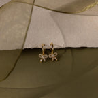 Flatlay of our Pave Bow Charm Hoops earrings on a soft fabric background