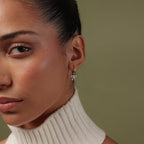 Close-up of a model wearing our Pave Bow Charm Hoops against a green background