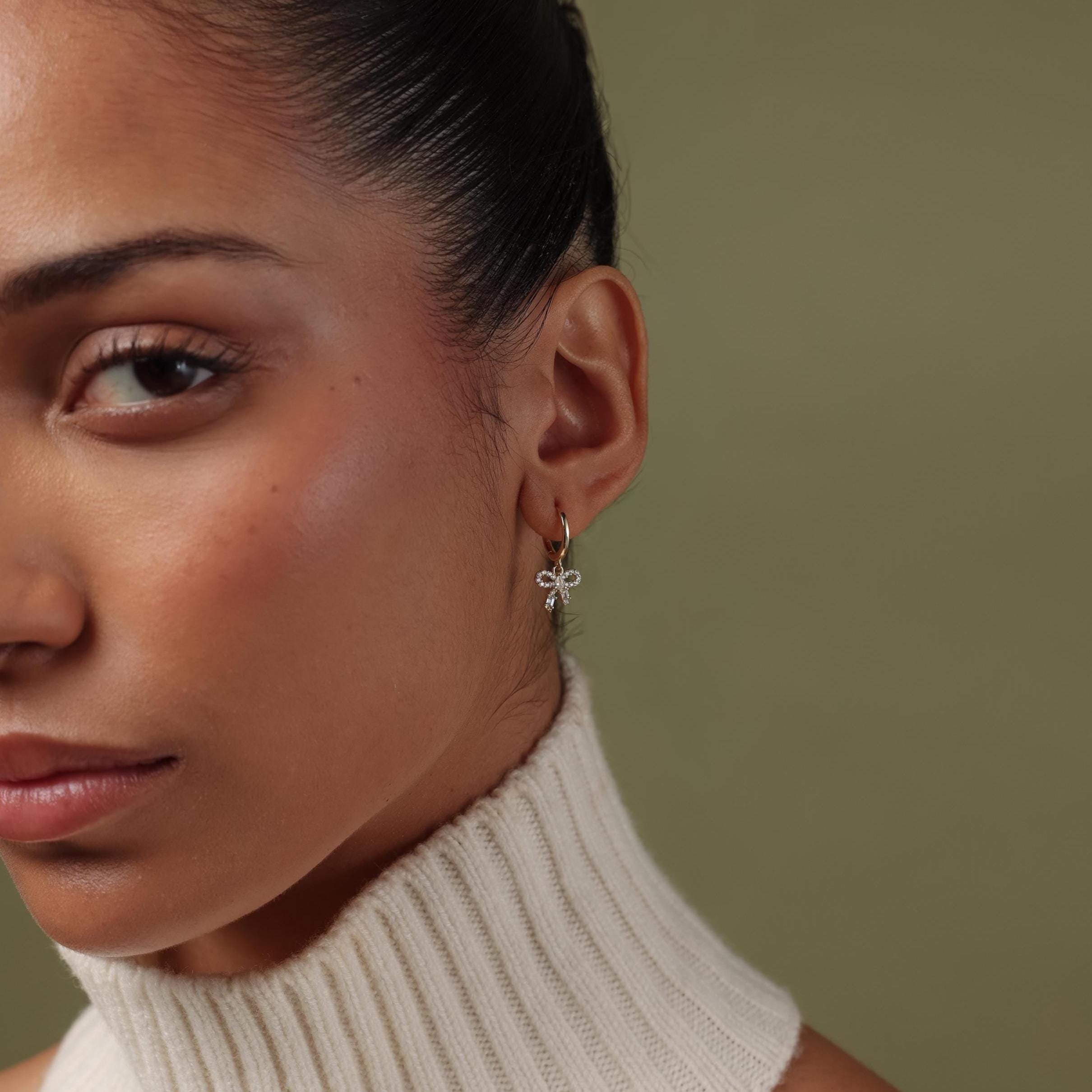 Close-up of a woman wearing our Pave Bow Charm Hoops against a neutral background