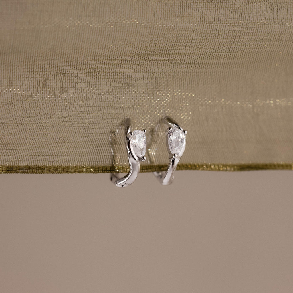 Flatlay of our Hammered Diamond Teardrop Hoops in Silver against a green ribbon