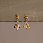 Gold Christmas tree earrings with Pink and Aquamarine gemstones on a beige fabric background