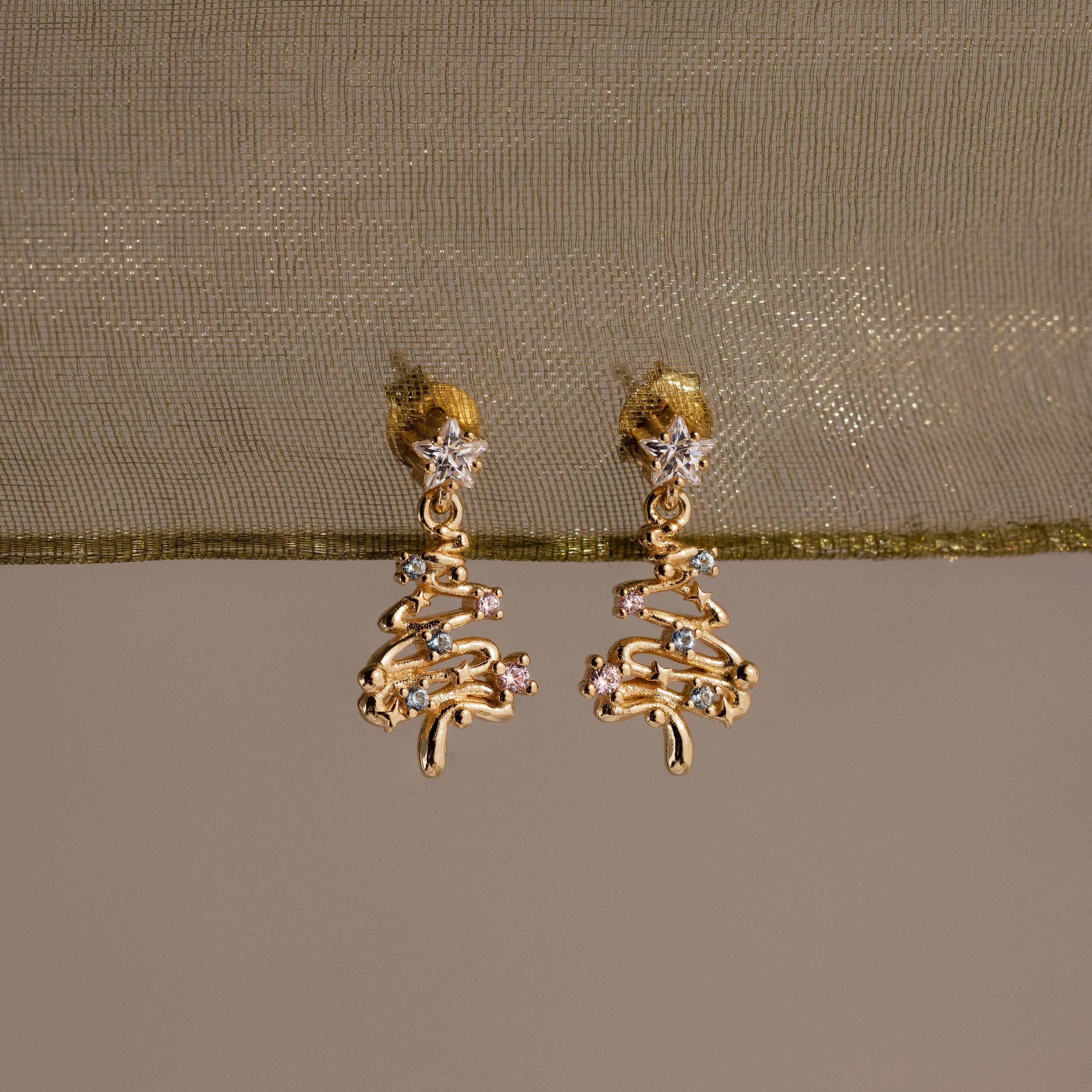 Gold Christmas tree earrings with Pink and Aquamarine gemstones on a beige fabric background