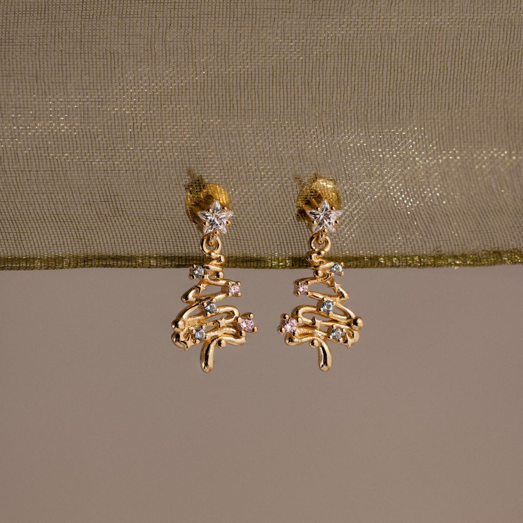 Gold Christmas tree earrings on a beige fabric background