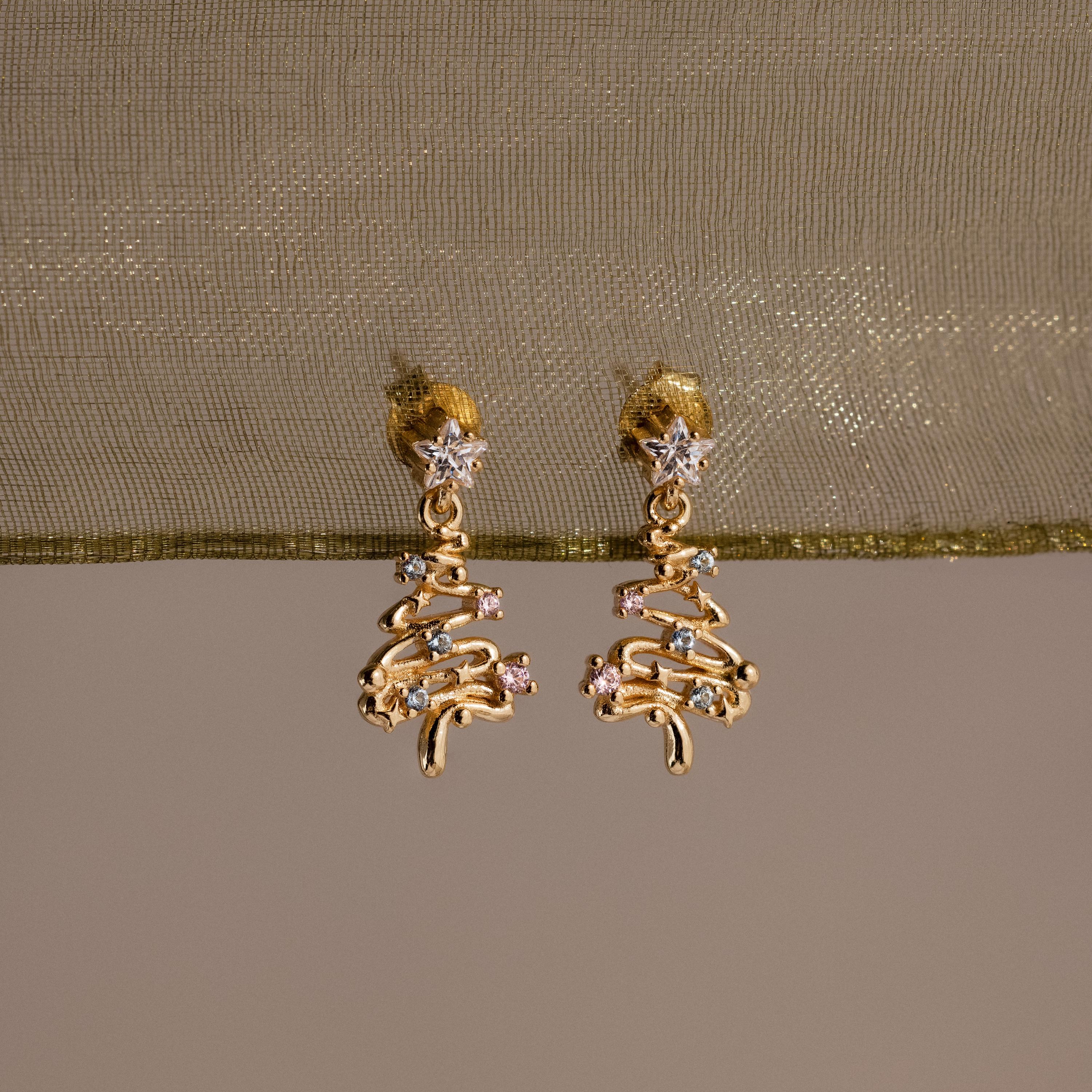 Gold Christmas tree earrings on a beige fabric background