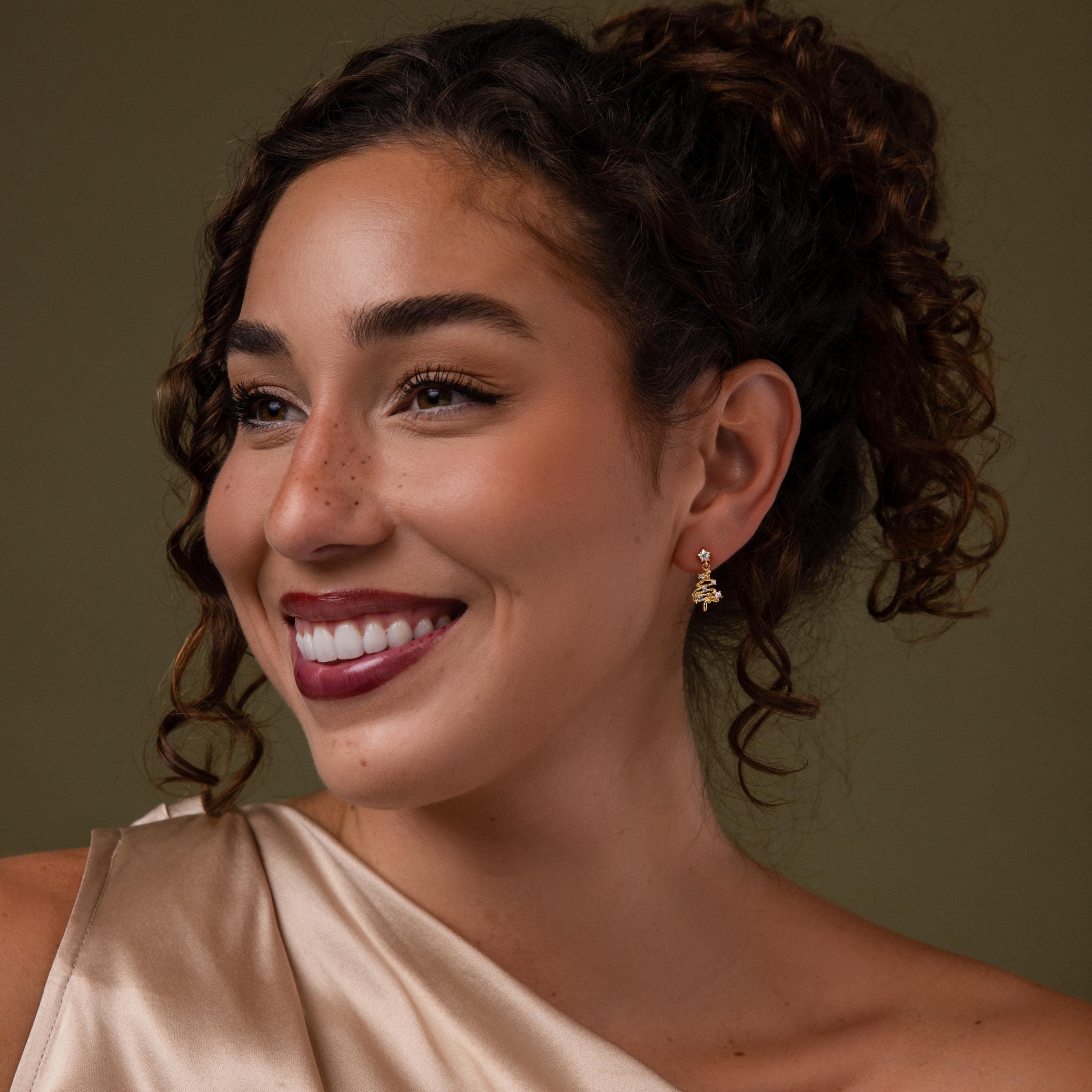 Model wearing our Holiday Tree Studs earrings against a green background