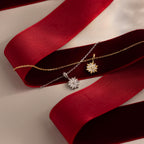 Flatlay of our Diamond Poinsetta Pendant Necklaces in Gold and Silver on a red ribbon