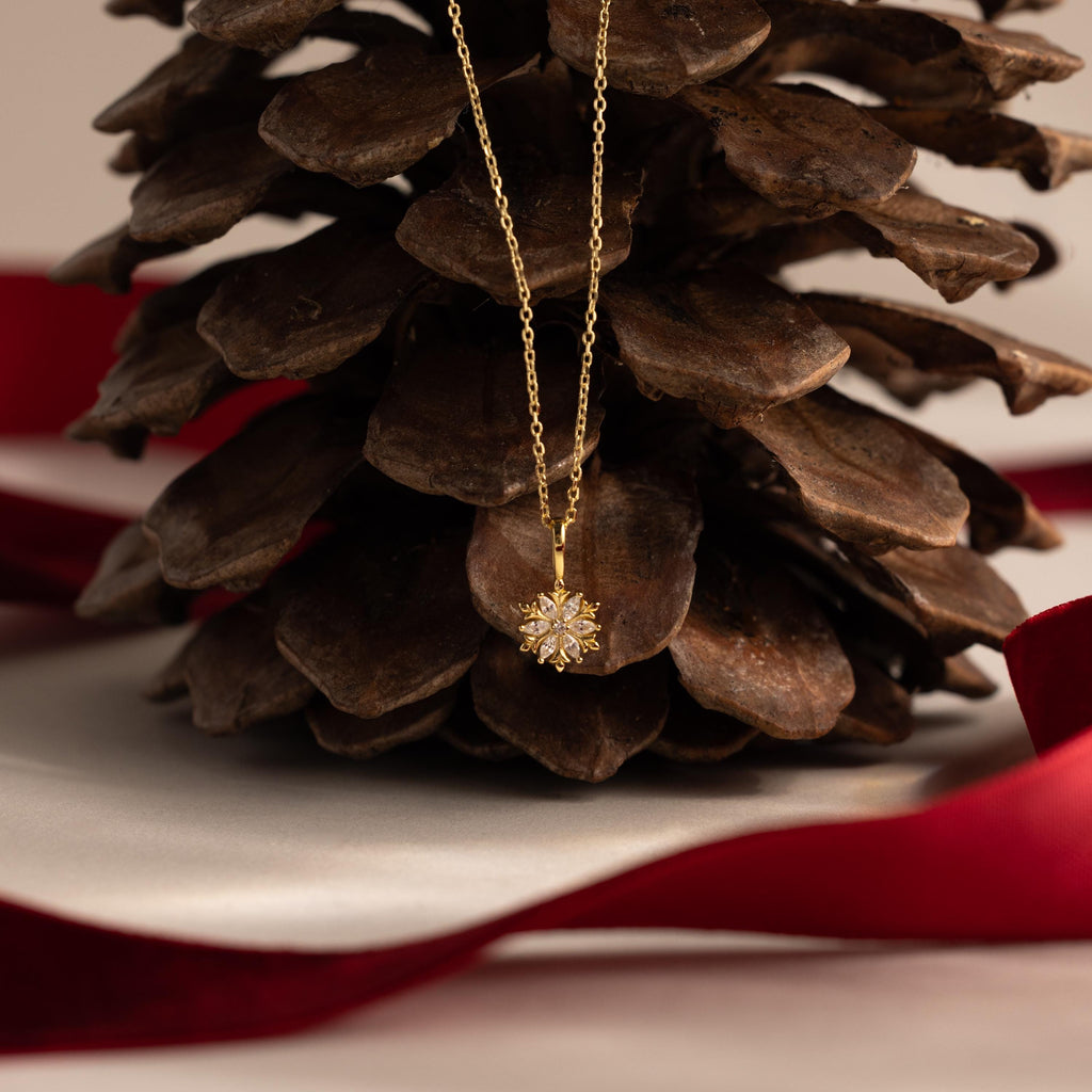 Flatlay of our Diamond Poinsettia Necklace on a pine cone with a red ribbon