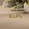 Birth Flower Stud Earrings with Amythest stones on a beige surface with green foliage in the background