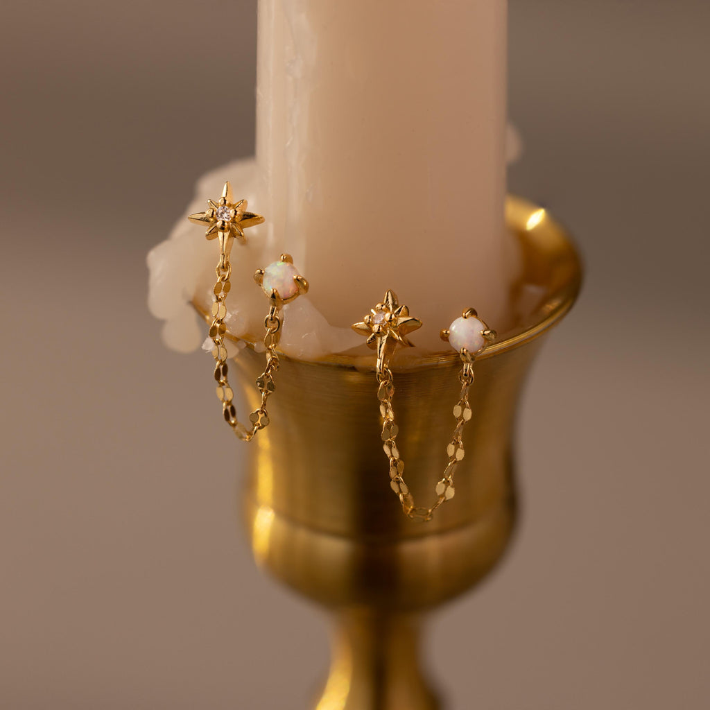 Opal & Star Duo Chain Studs in Gold against a beige candle
