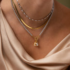 Model wearing a layered necklace look with our Eternity Pearl Necklace. Herringbone necklace and Smoky Pearl Clasp Necklace with our Mother of Pearl Initial Charm and Teardrop Birthstone Charm attached to the clasp.