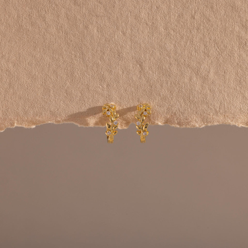 Photo of our Diamond Leaf Hoops in 18K Gold on a beige background