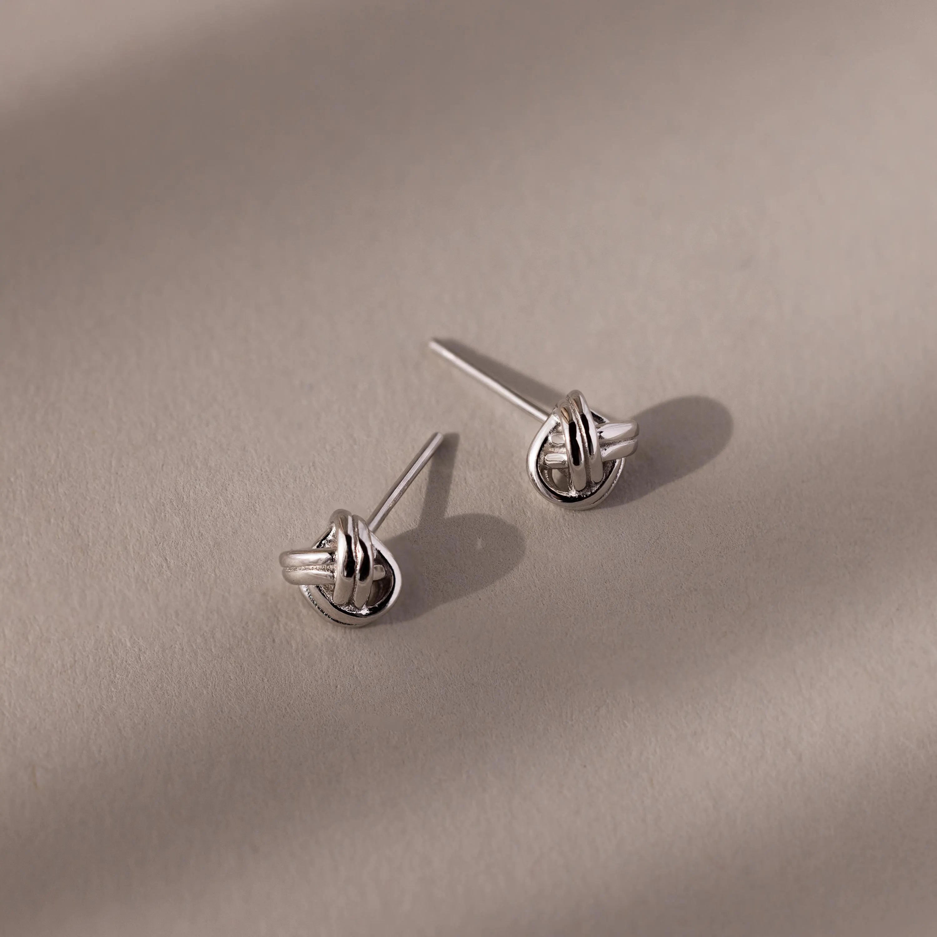 Pair of silver knot earrings on a beige background